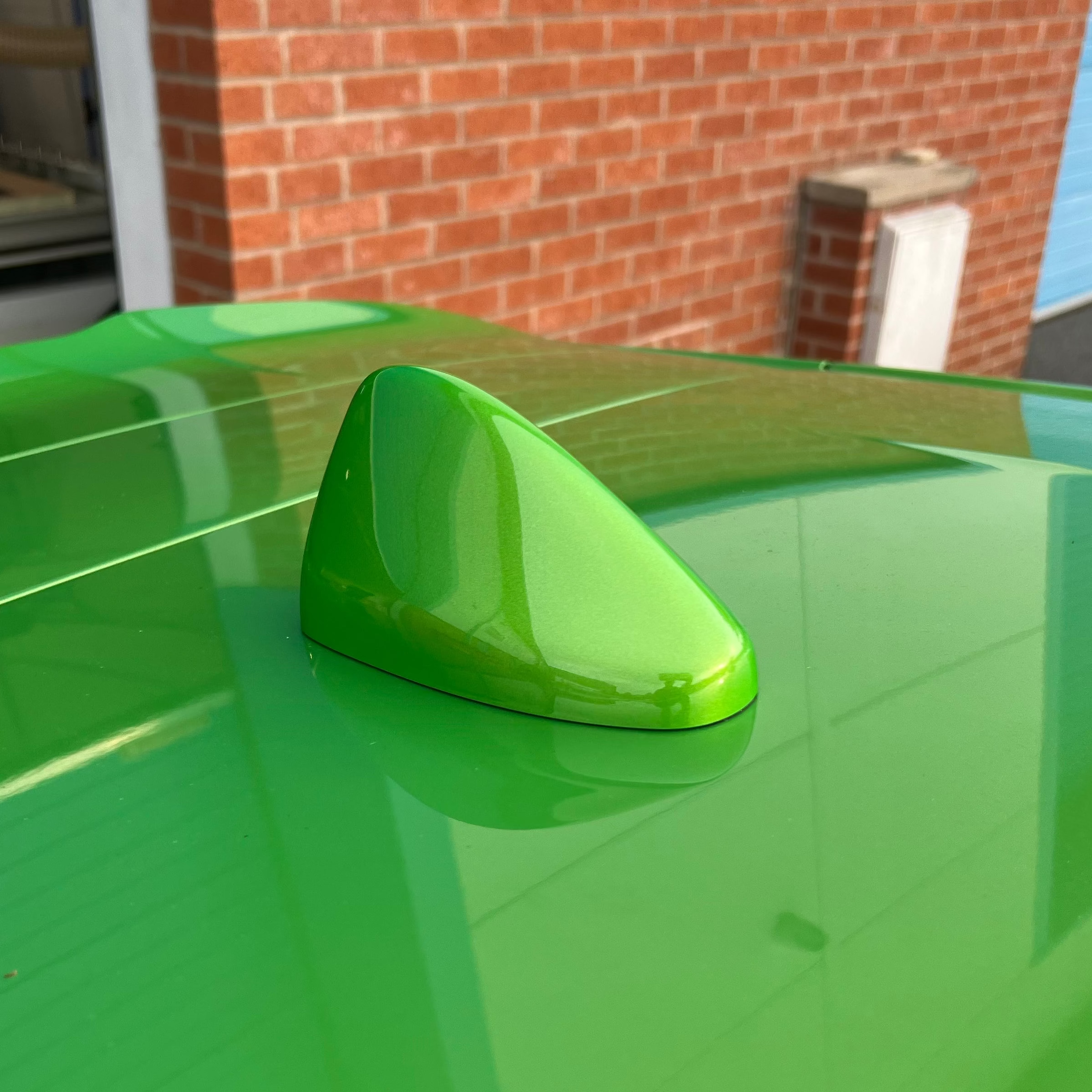 Green car Shark Fin aerial on a green car with a brick building in the background