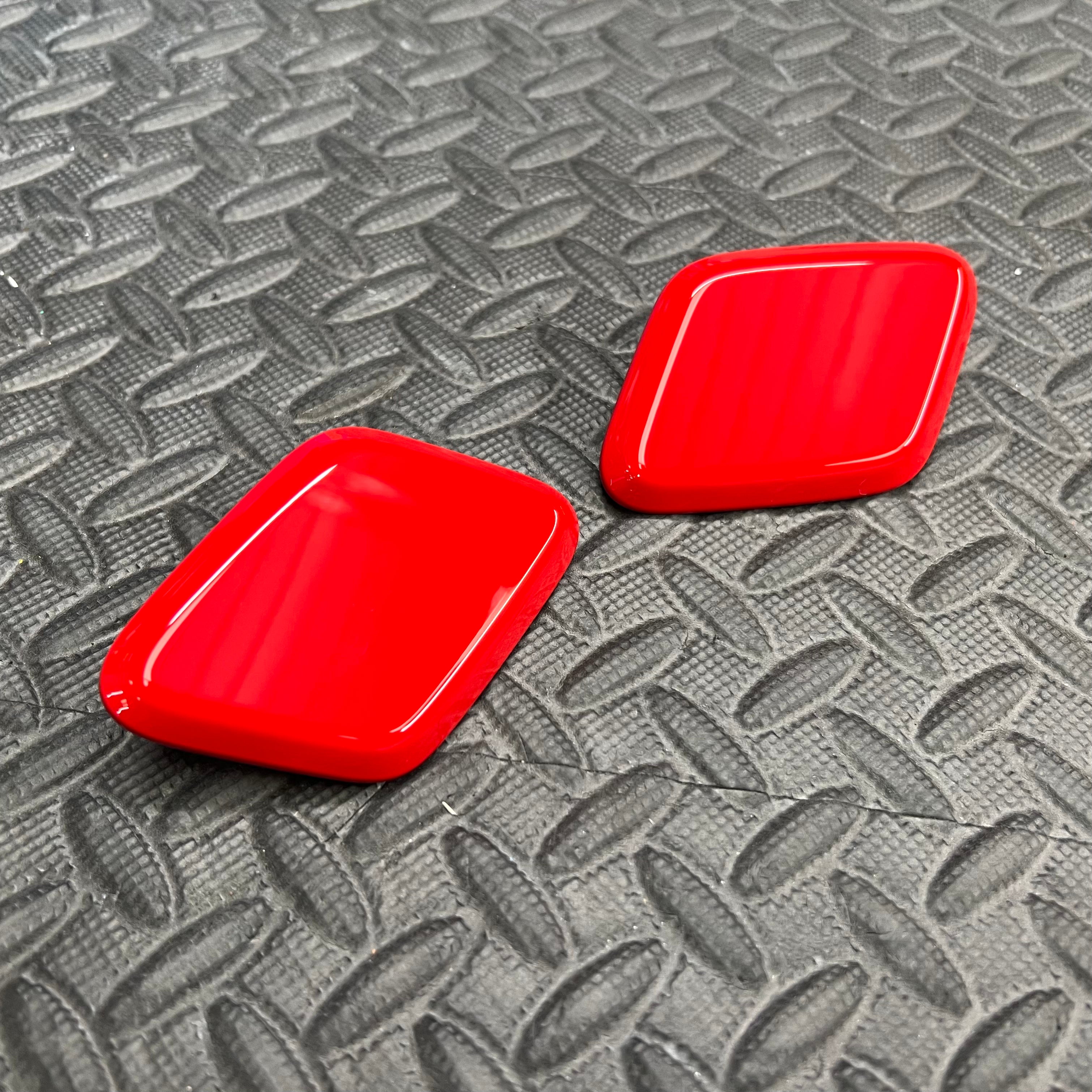 A pair of red Ford headlight washer covers placed on a textured surface.